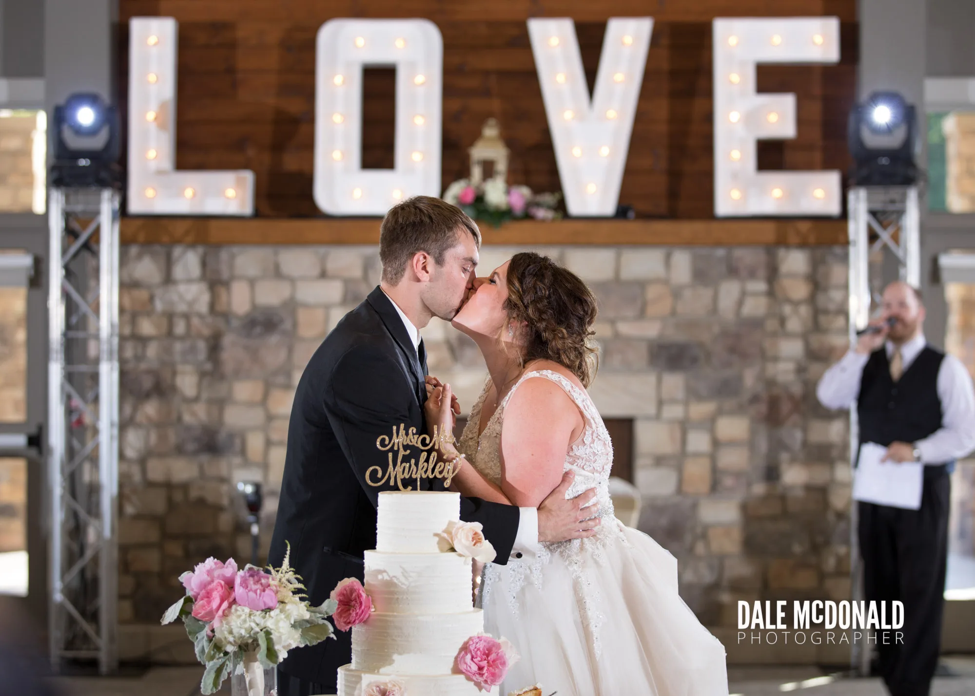 couple kissing in front of cake with rock the house entertainment wedding DJ announcing