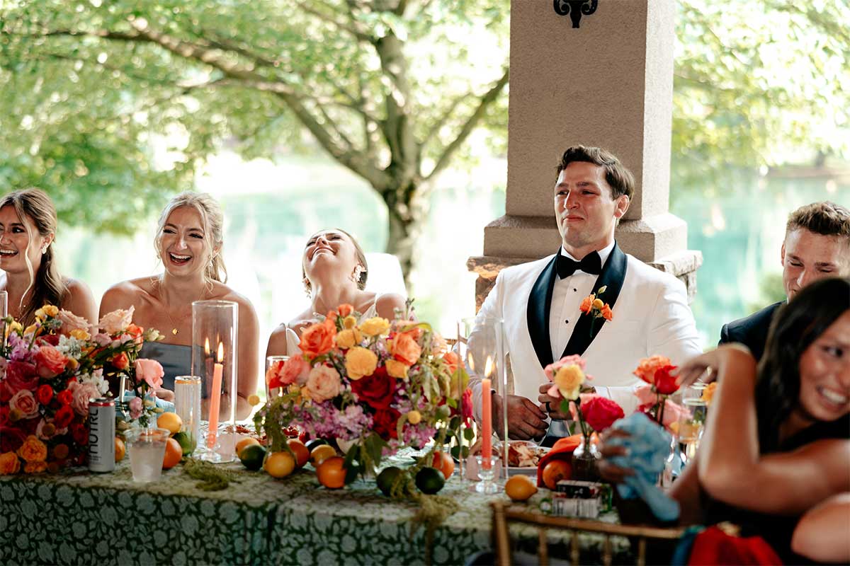 bride, groom, and bridal party laughing during dinner